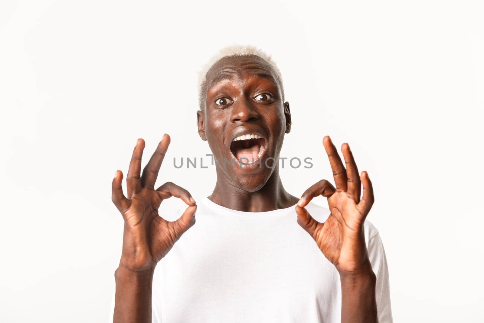 Close-up of excited attractive african-american blond guy express amazement, showing okay gesture in approval, standing white background.