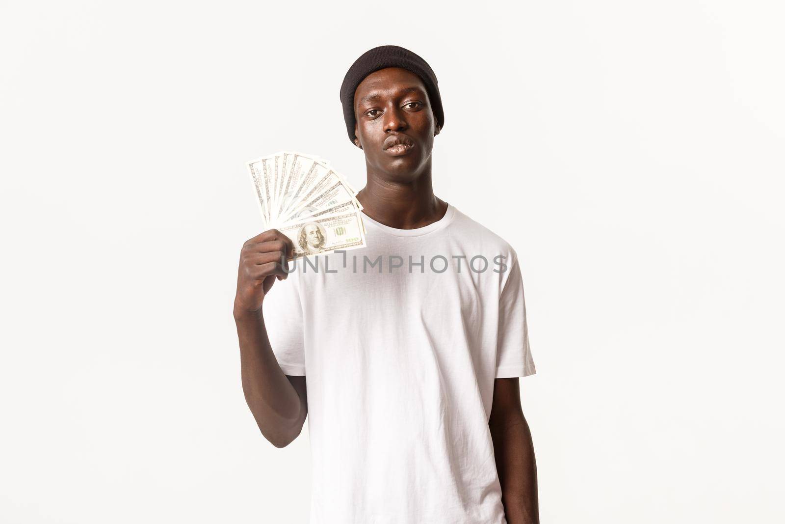 Portrait of sassy and cool african-american rich guy showing money and looking at camera with serious face, white background.