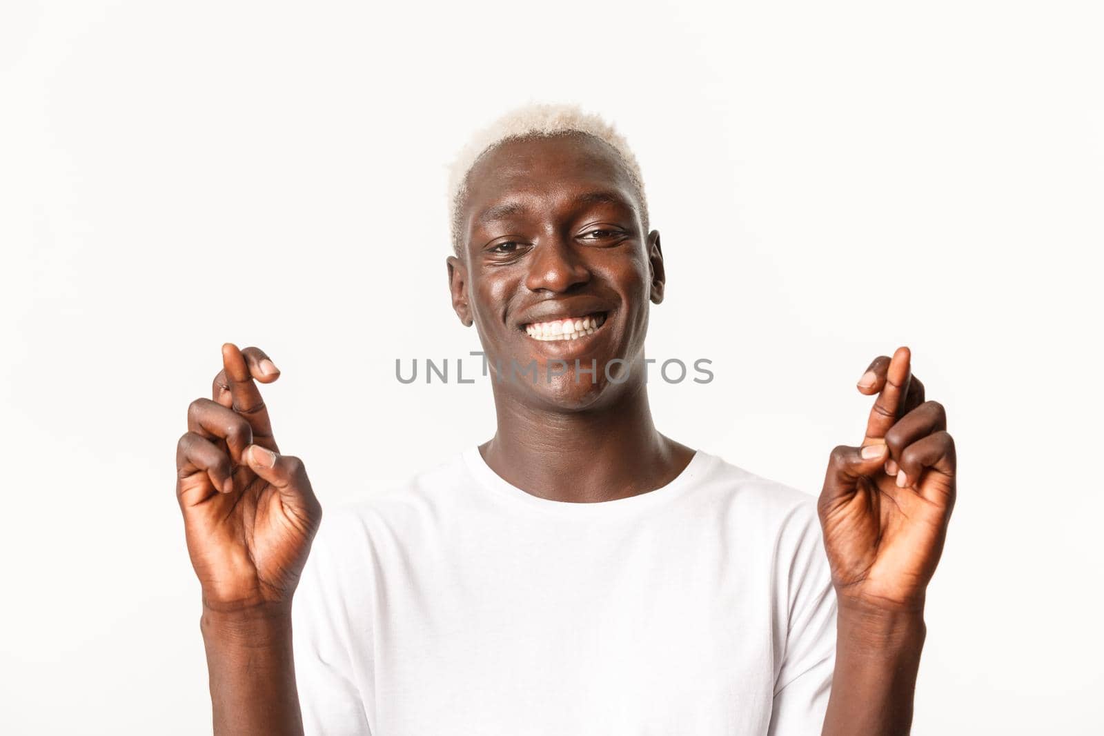 Close-up of happy and hopeful african-american handsome blond guy, making wish, smiling optimistic and cross fingers good luck, standing white background.