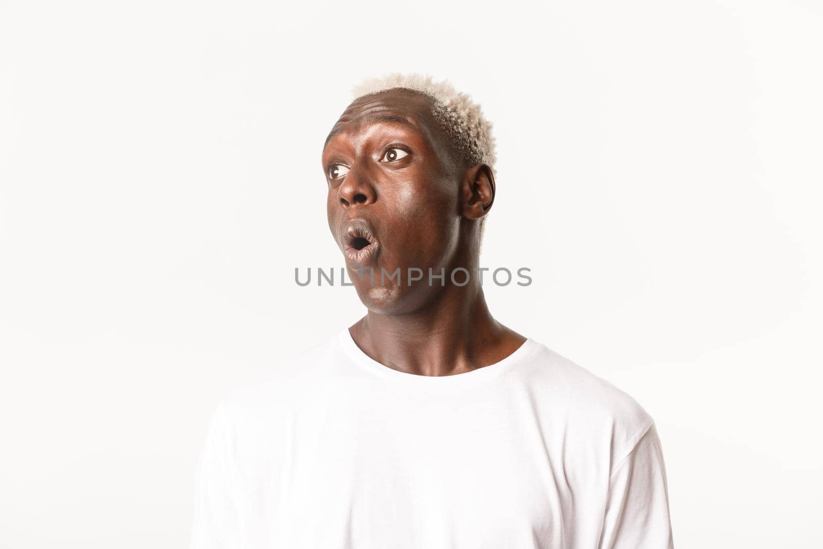 Close-up of surprised and amazed handsome african-american blond man, drop jaw wondered and looking left, saying wow, standing white background.