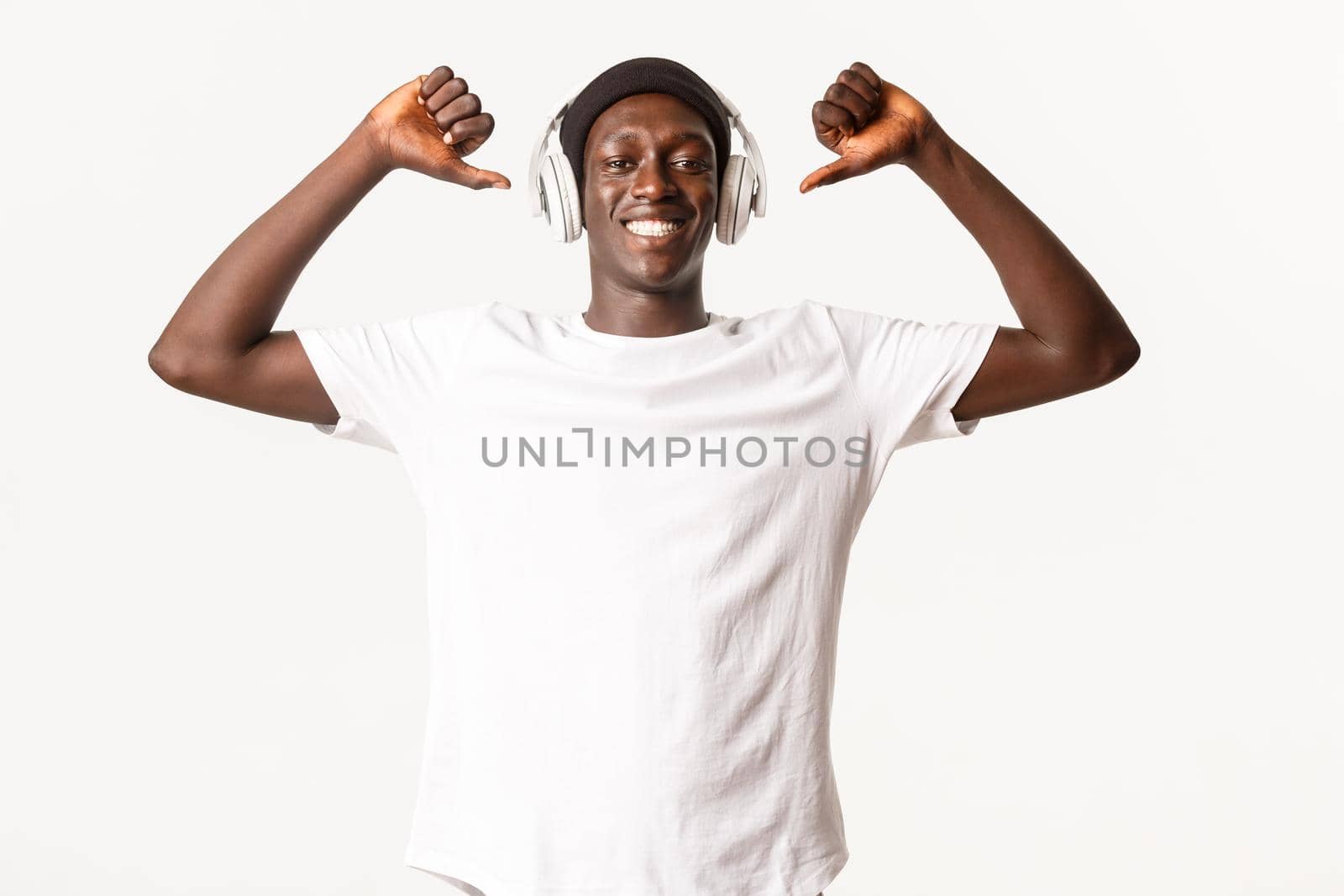 Portrait of happy and pleased african-american young male, pointing fingers at himself with pleased smile, white background.