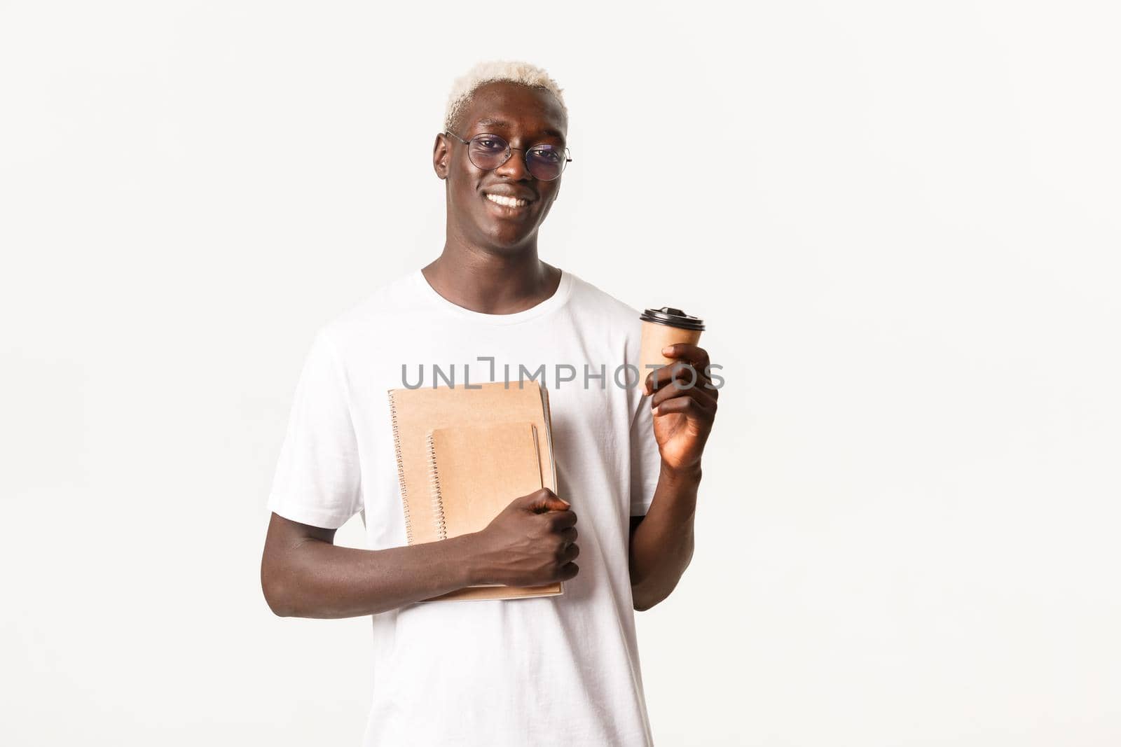 Portrait of handsome stylish african-american guy with blond hair, going to college, wearing glasses, holding cup of coffee and notebooks, standing white background.