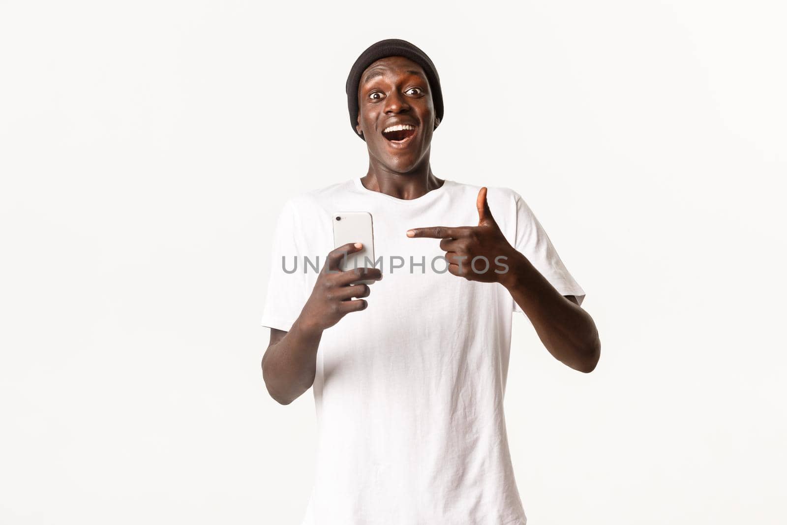 Portrait of young excited african-american guy recommending smartphone app, pointing finger at mobile phone with amazed and happy face.