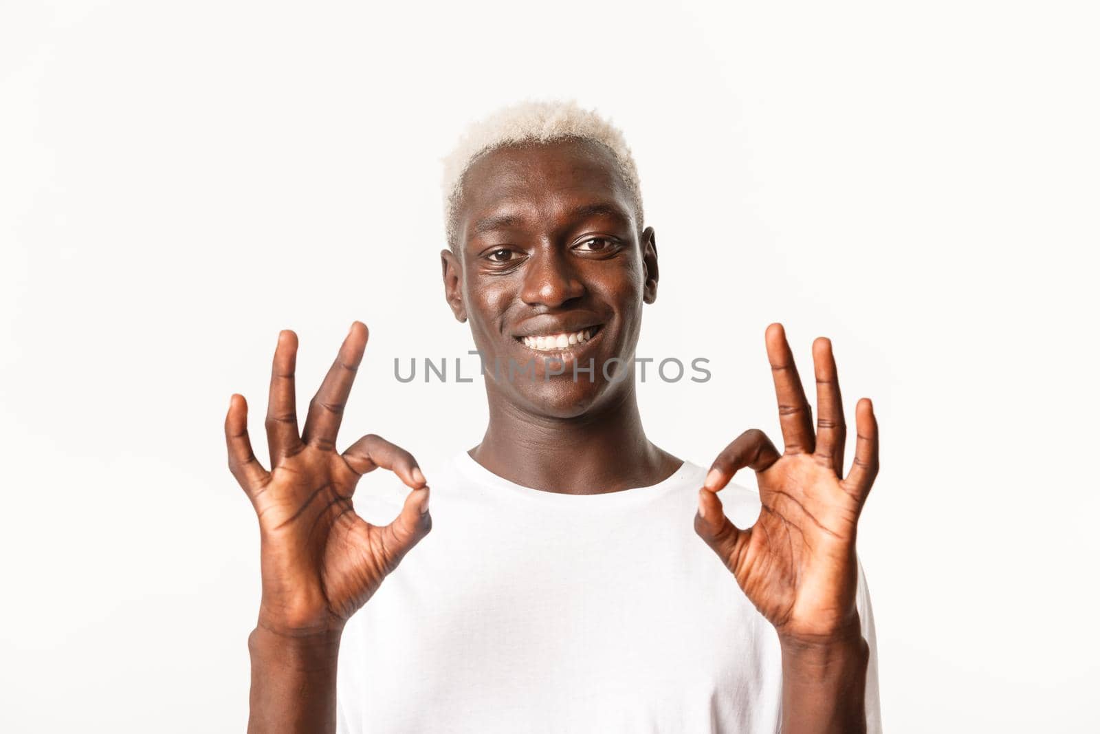 Close-up of satisfied attractive african-american blond guy showing okay gesture and smiling, like and approve, standing over white background.