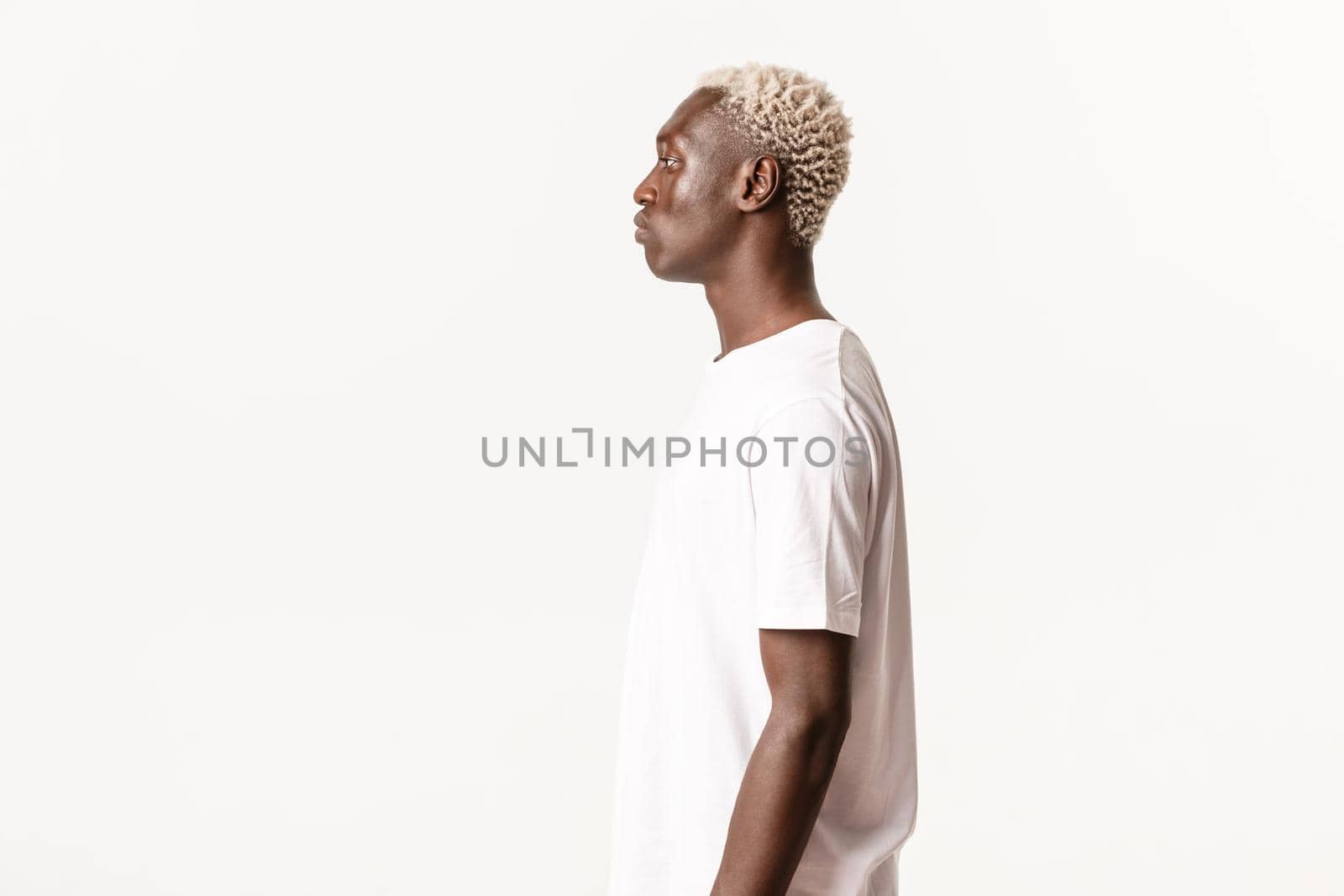 Profile of serious-looking african american blond man looking left, standing over white background.