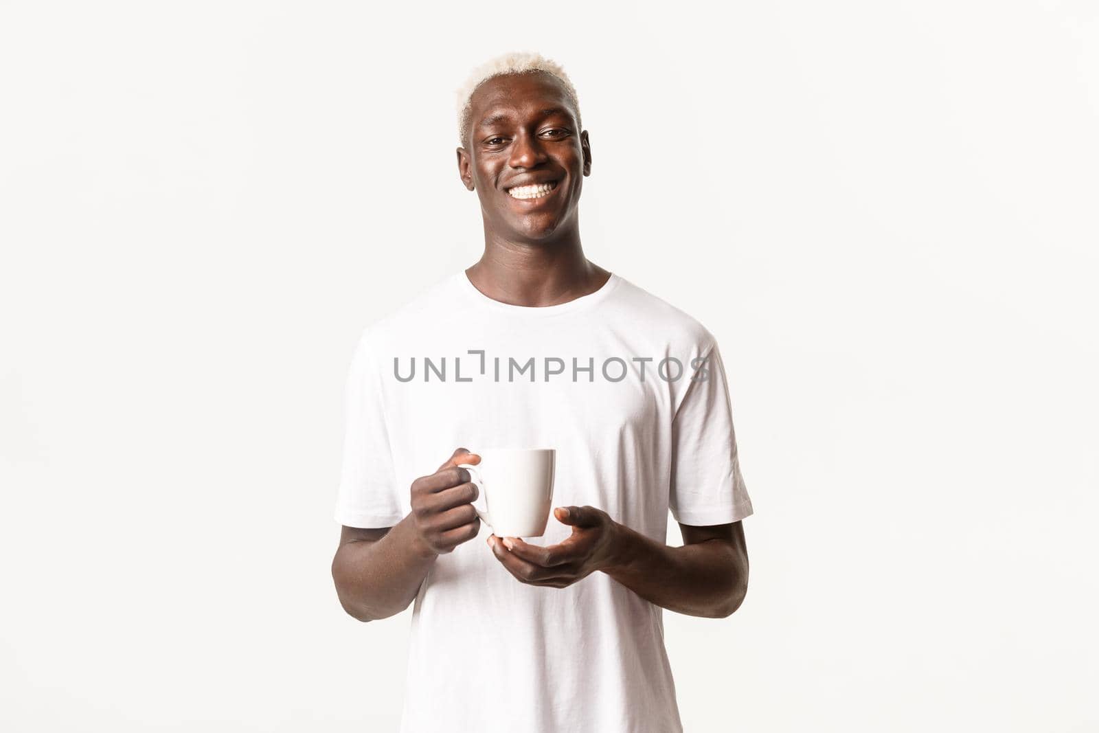 Portrait of happy smiling african-american blond man, looking satisfied, drinking coffee or tea, standing over white background.