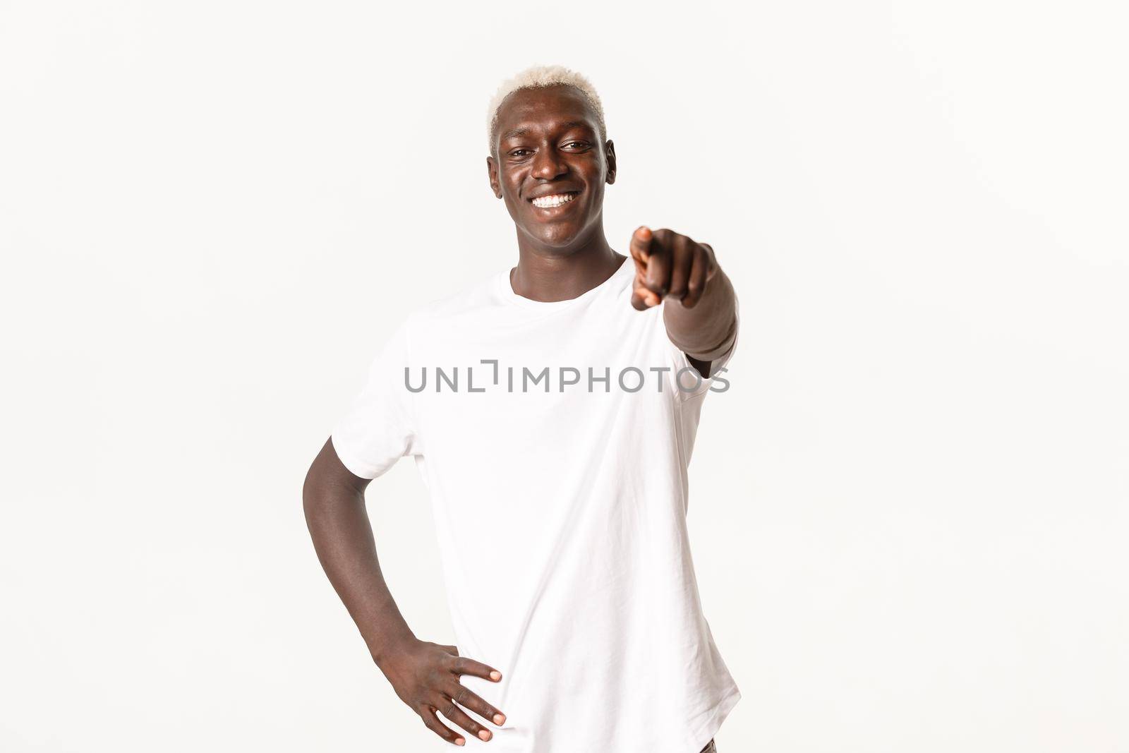 Portrait of handsome happy african-american man, smiling pleased and pointing finger at camera, standing white background.