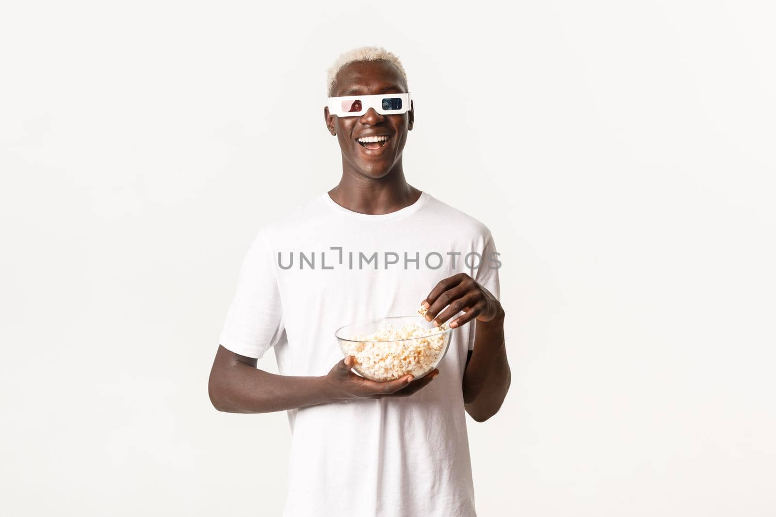 Portrait of carefree smiling african-american guy, watching movie in 3d glasses and eating popcorn, enjoying cinema, standing white background.