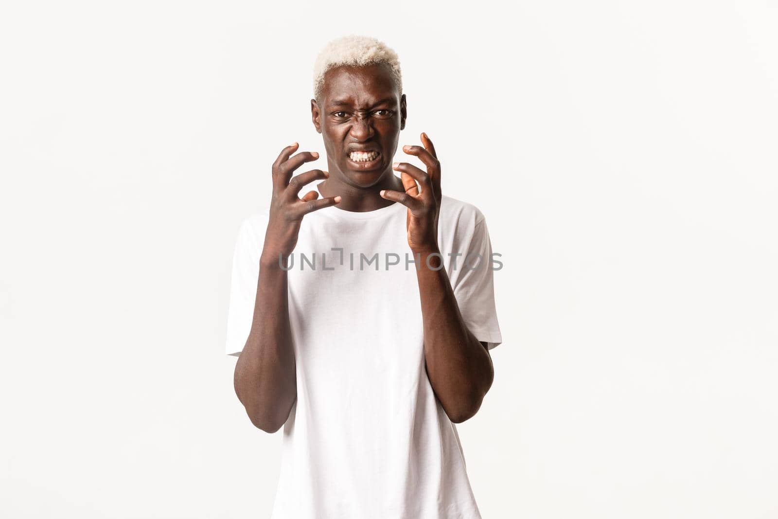 Portrait of angry african-american blond man, clenching hands and looking hateful, feeling outraged or bothered, standing over white background.