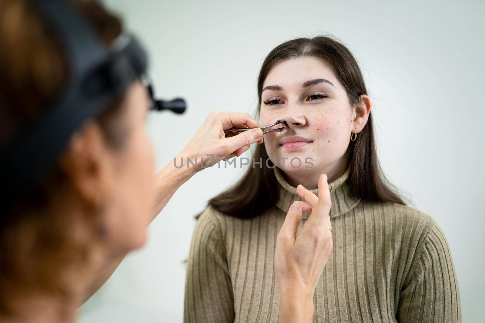 Female ENT doctor examines patient's sinuses with medical instrument in modern clinic. Otorhinolaryngologist checks the patient's girl's nose for diseases, allergies and curvature of the nasal septum.