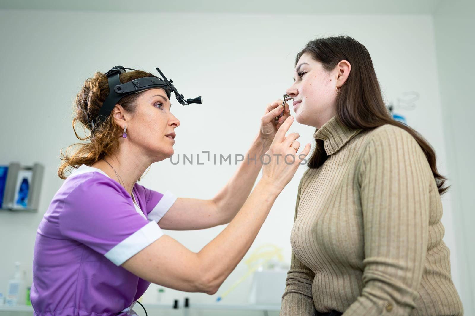 Professional female doctor otorhinolaryngologist doing nose examination with otoscope in modern hospital. Nasal congestion, sinusitis, allergy concept. Woman ENT doctor and patient in office clinics.