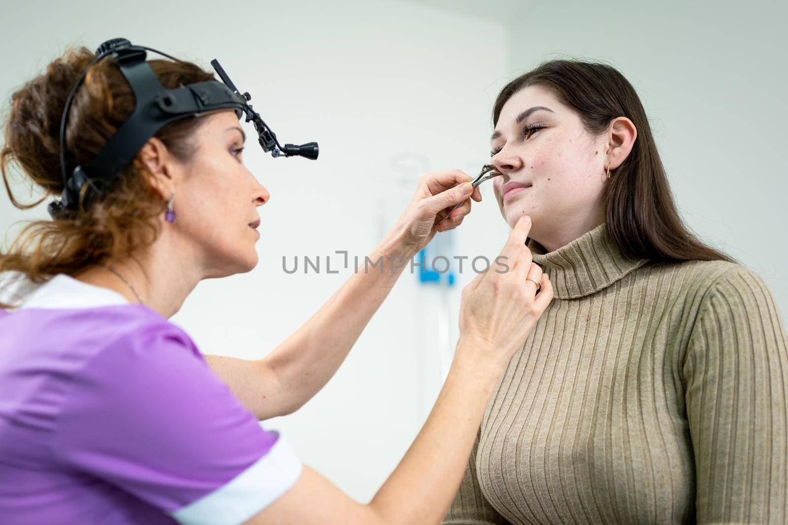 Otolaryngology concept. Positive woman otorhinolaryngologist checking nose with otoscope of his patient at hospital. Nasal congestion, sinusitis, allergy concept. Female patient at modern ENT clinic by Tomashevska