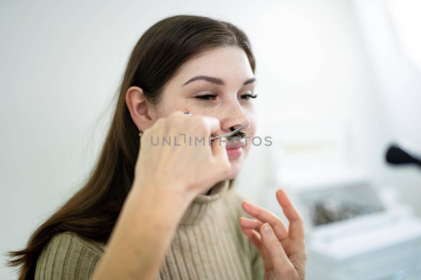 Female ENT doctor examines patient's sinuses with medical instrument in modern clinic. Otorhinolaryngologist checks the patient's girl's nose for diseases, allergies and curvature of the nasal septum.