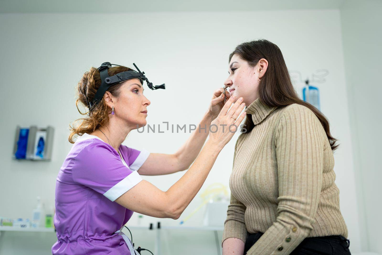 Female ENT doctor examines patient's sinuses with medical instrument in modern clinic. Otorhinolaryngologist checks the patient's girl's nose for diseases, allergies and curvature of the nasal septum by Tomashevska