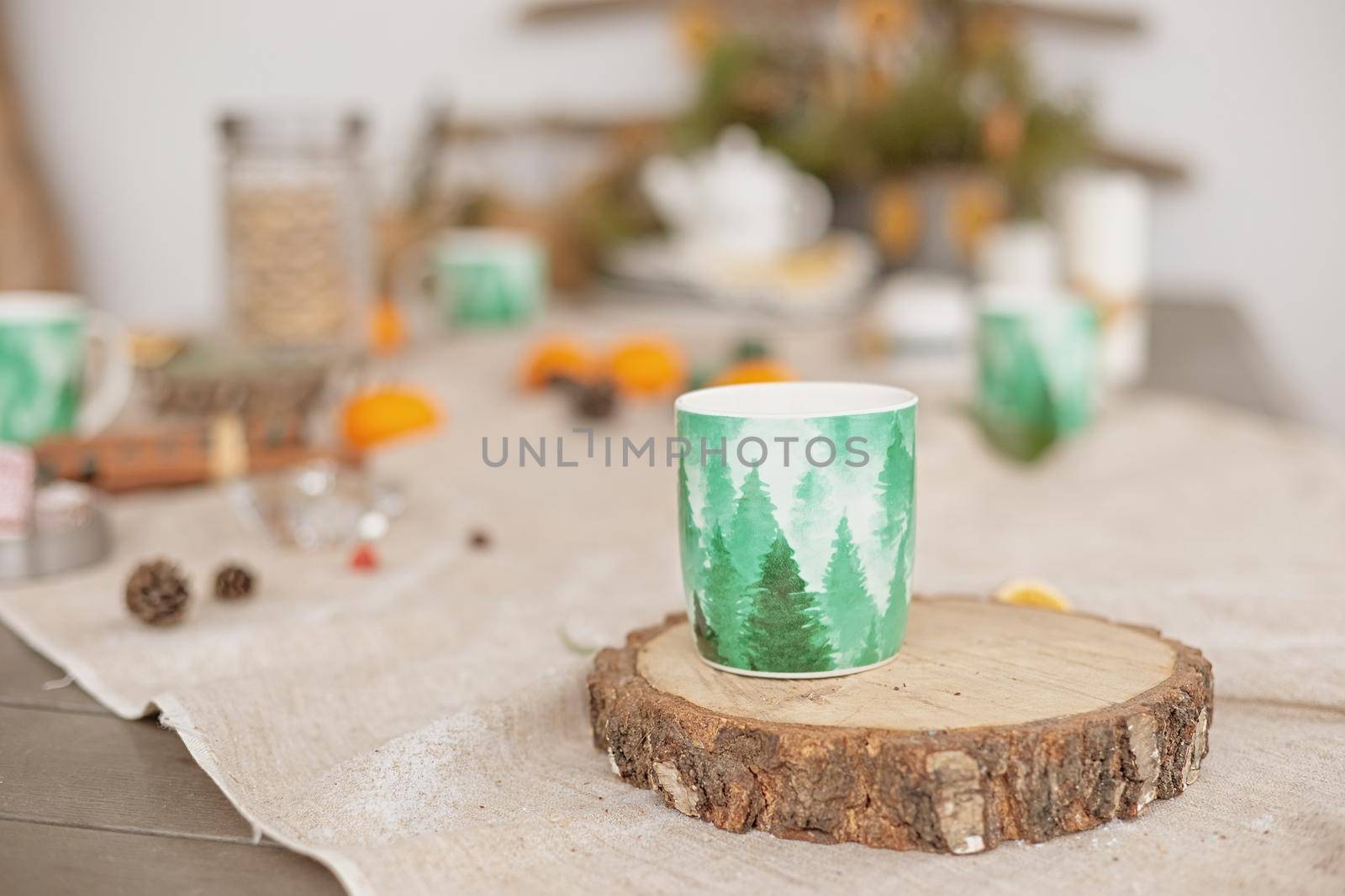 Winter table decor , on a linen tablecloth there is a green mug of hot drink on a tree cut.