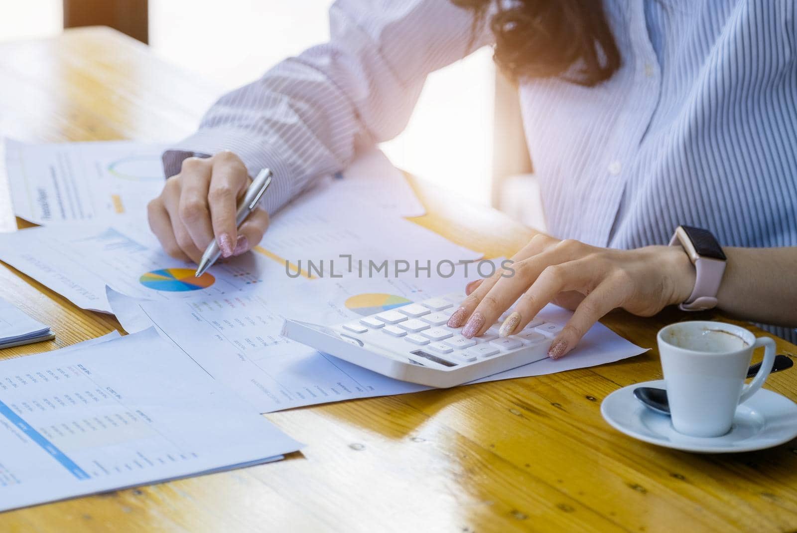 A businesswoman uses a calculator to calculate her last quarter's earnings budget to plan her business investments for the coming year. by Manastrong