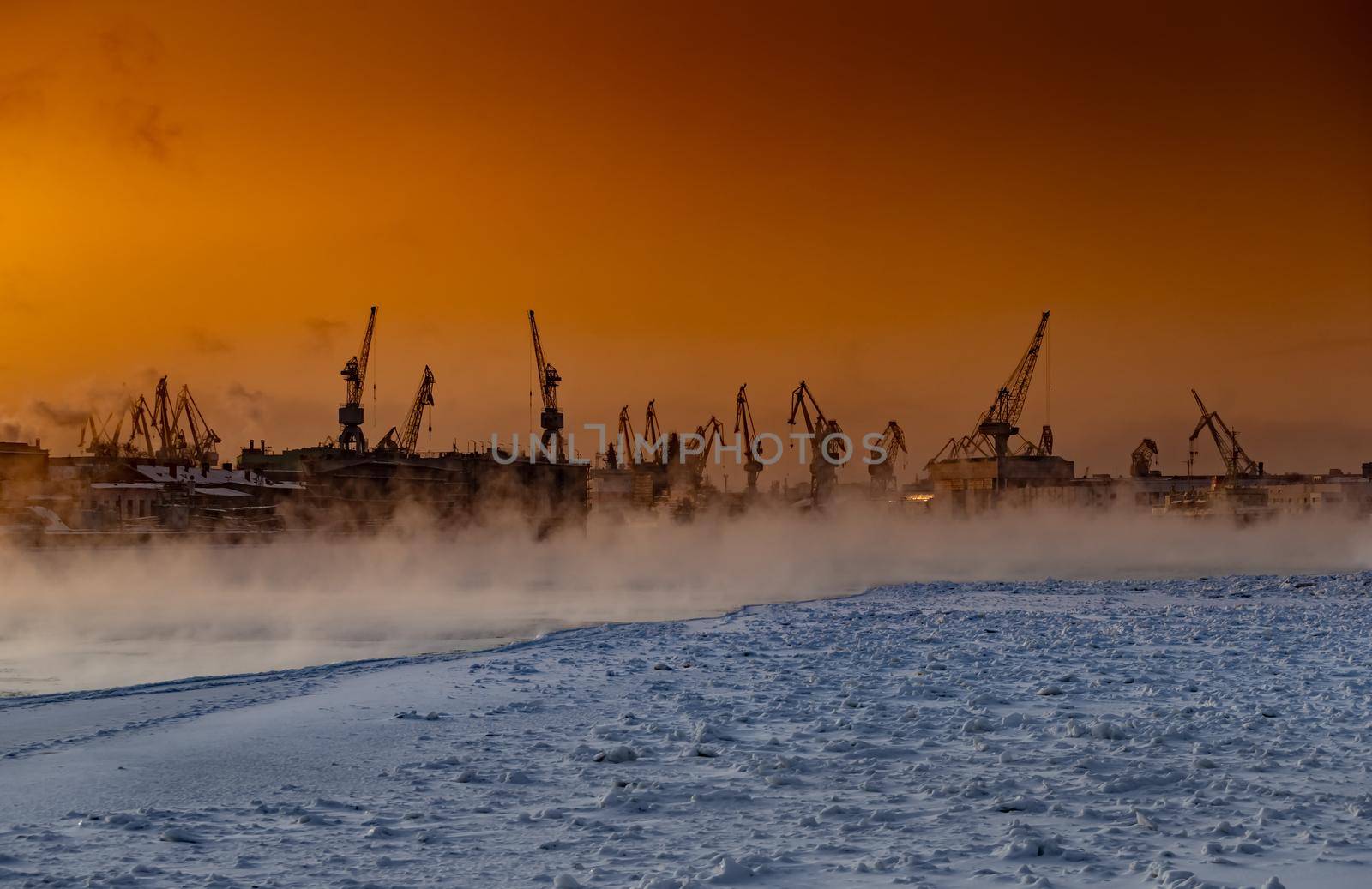 The construction of nuclear icebreakers at magic sunset, cranes of of the Baltic shipyard in a frosty winter day, steam over the Neva river, smooth surface of the river, sky of orange color. High quality photo