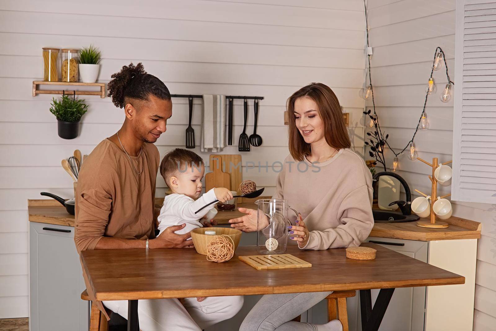 Beautiful young family, in cozy brown clothes, sitting at a table in the kitchen by Zakharova