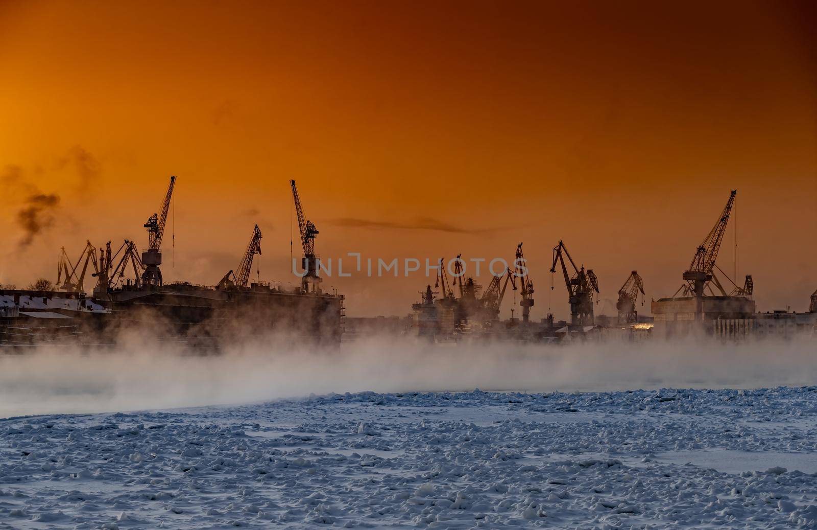 The construction of nuclear icebreakers at magic sunset, cranes of of the Baltic shipyard in a frosty winter day, steam over the Neva river, smooth surface of the river, sky of orange color. High quality photo