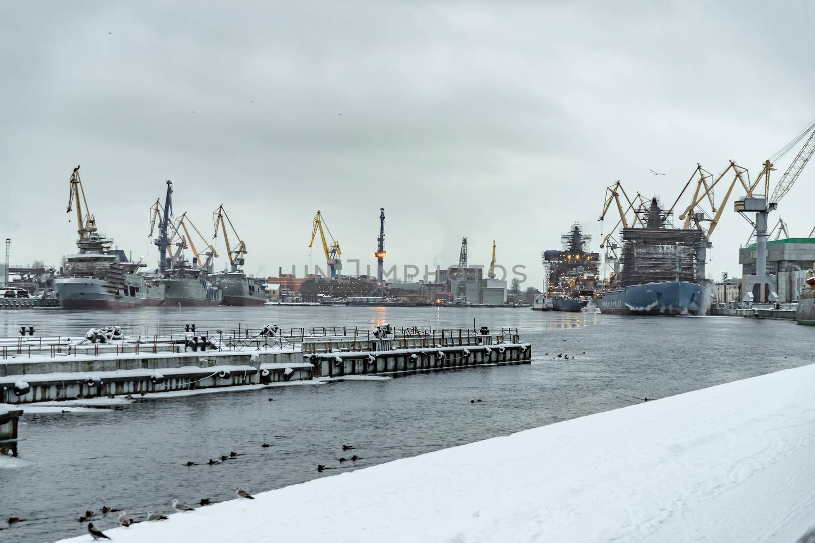 Russia, St. Petersburg, 05 February 2021: The construction of nuclear icebreakers, cranes of of the Baltic shipyard in a frosty winter day, steam over the Neva river, smooth surface of the river. High quality photo