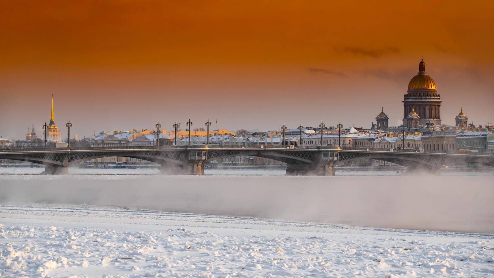 Winter panoramic view of St. Petersburg at sunset, Isaac cathedral and Blagoveshenskiy bridge on background, steam over frozen Neva river, sky of orange color. High quality photo