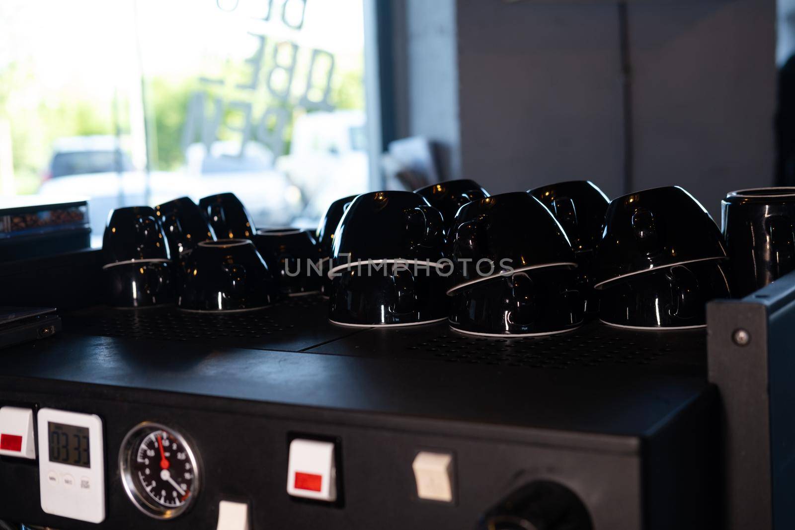 Pile of empty clean black coffee cups mugs on shelf or coffee machine in cafe indoors.