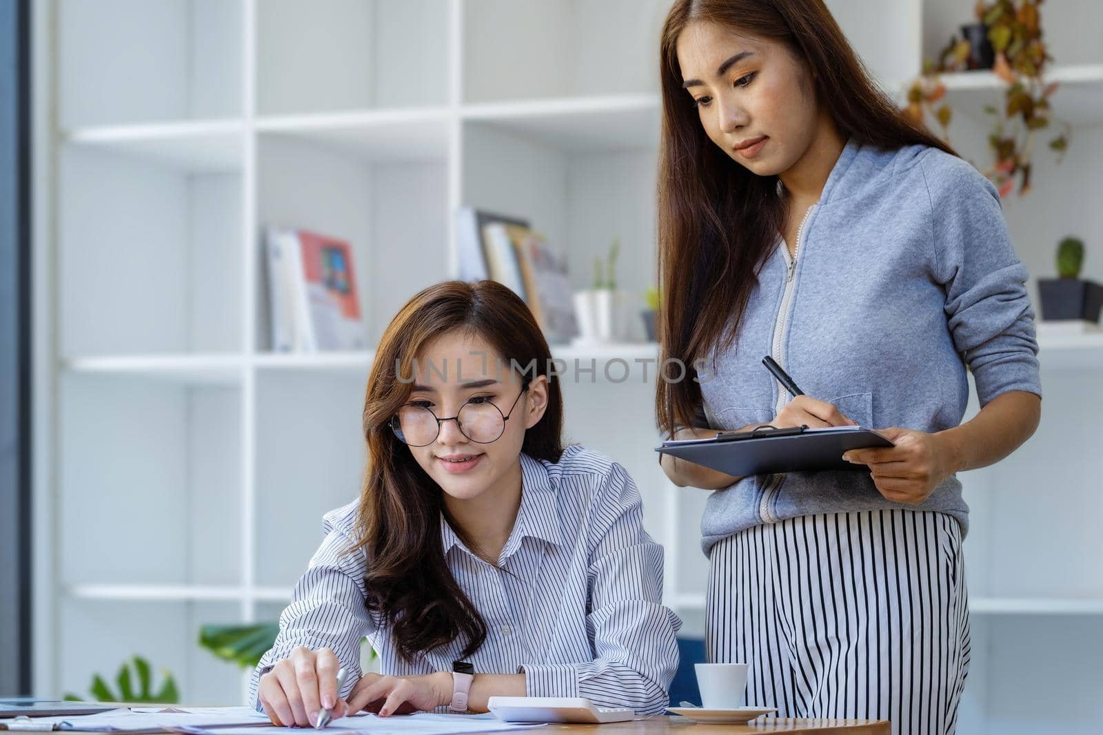 Businesswomen and colleagues are using budget document to calculate last quarter earnings of the year to plan financial investments for the coming year. by Manastrong