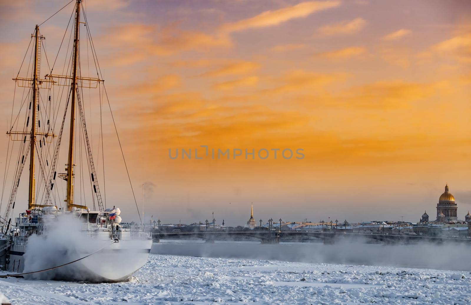 Winter panoramic view of St. Petersburg at sunset, Isaac cathedral and Blagoveshenskiy bridge on background, steam over frozen Neva river, sky of orange color. High quality photo