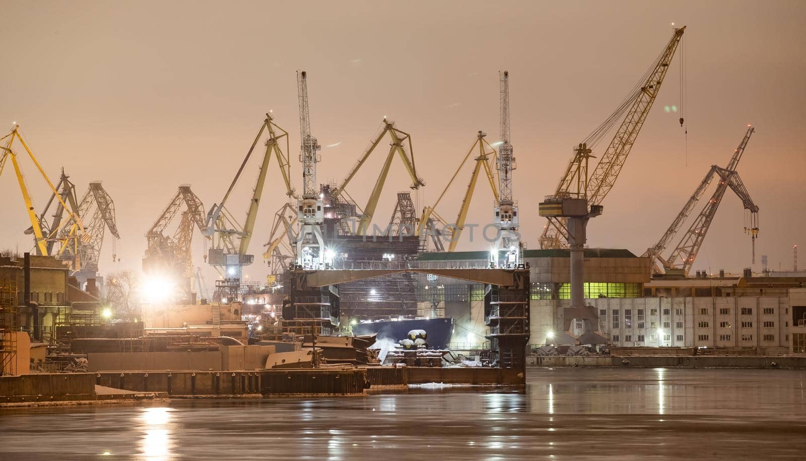 The construction of nuclear icebreakers at night, cranes of of the Baltic shipyard in a frosty winter day, steam over the Neva river, smooth surface of the river, fog. High quality photo