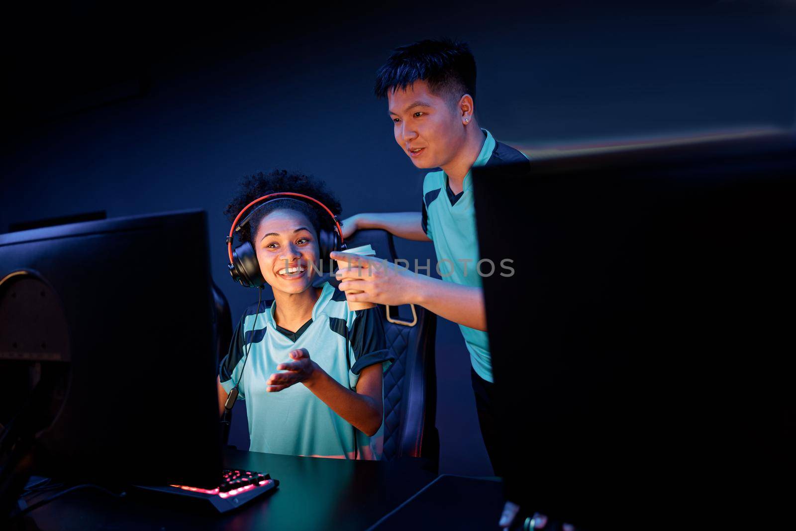 Cheerful African female cybersport gamer discussing game development with teammate while participating in online gaming tournament in computer club