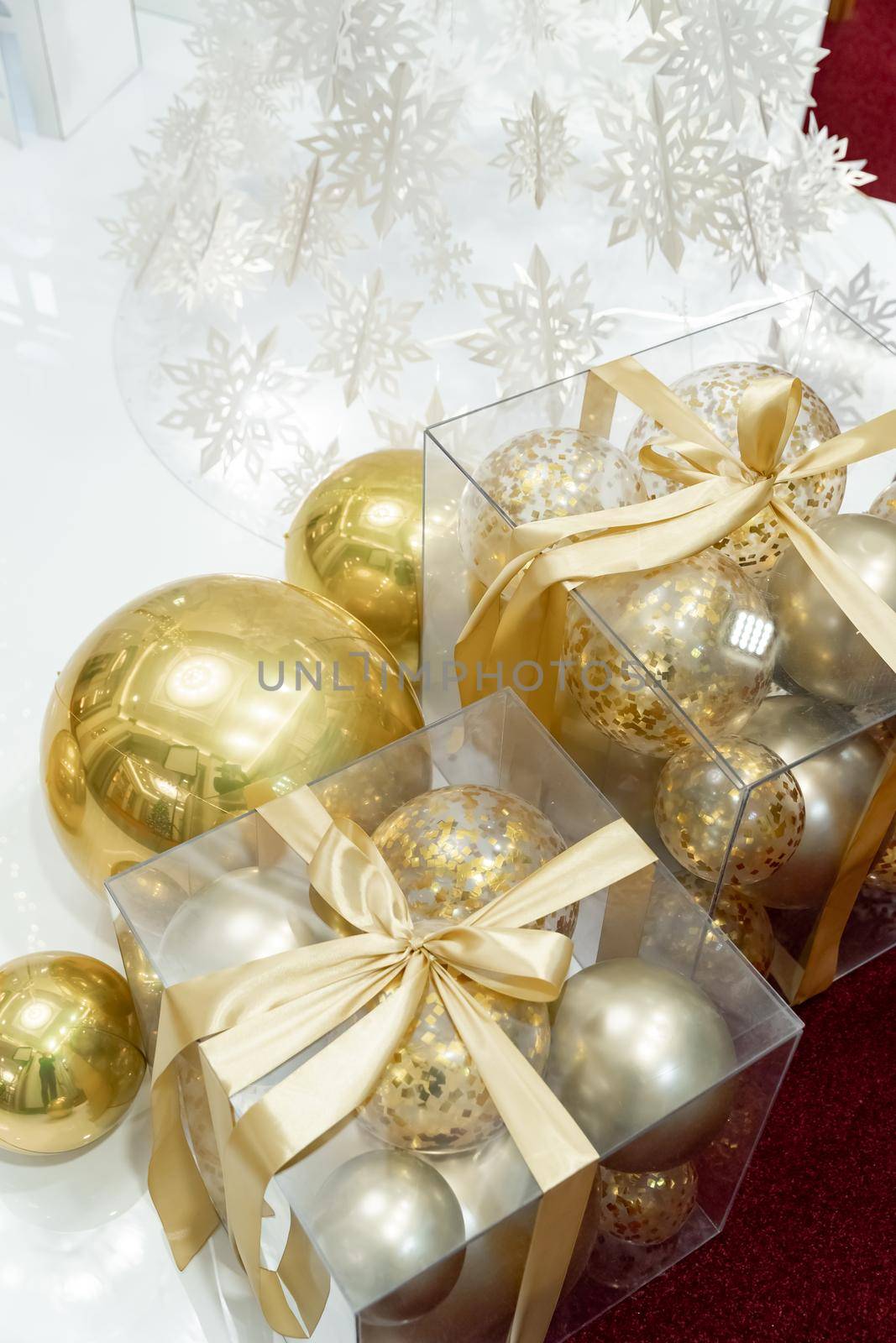 Christmas decoration in the form of gold Christmas balls in a package with a gold ribbon, white paper snowflakes, red carpet. High quality photo