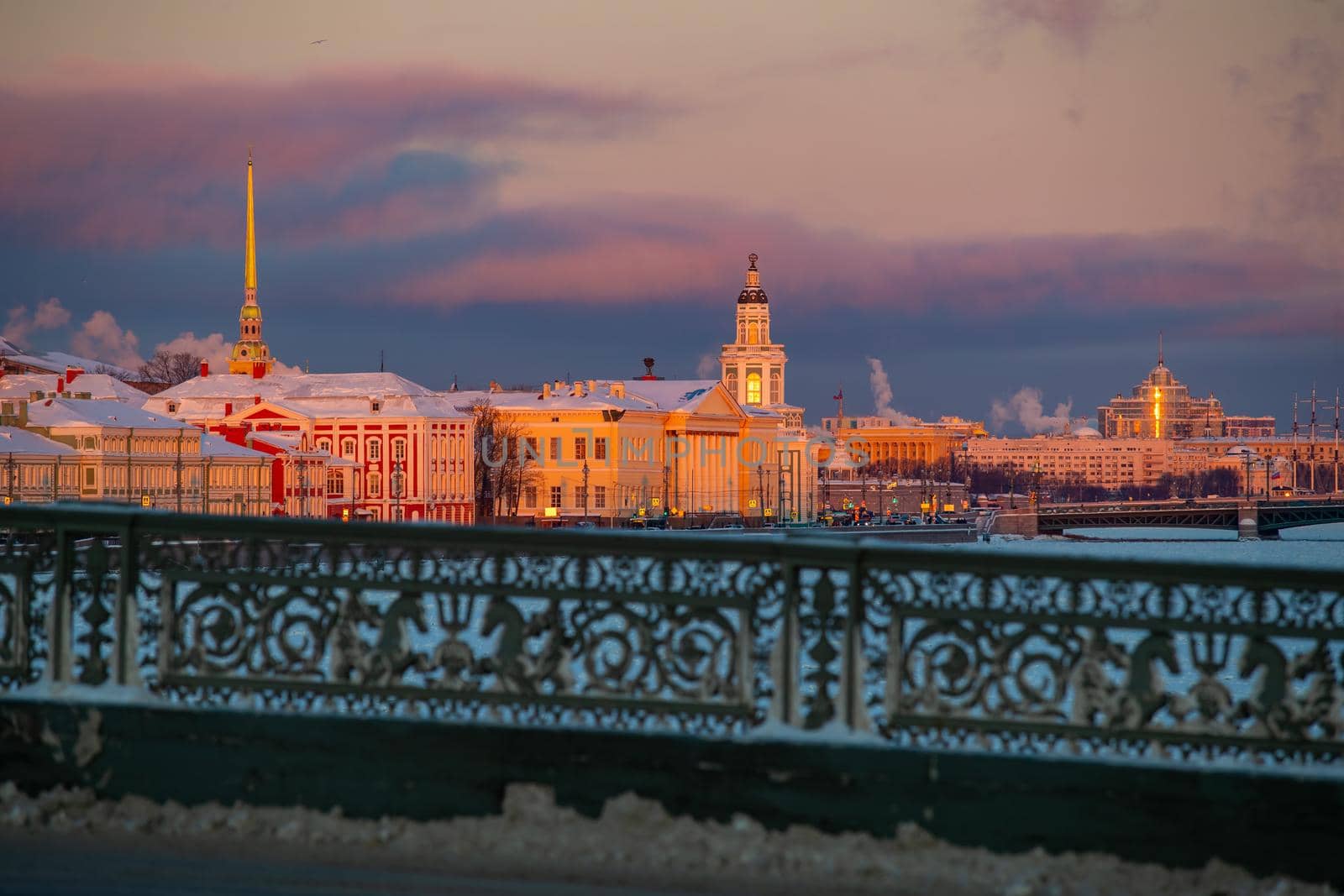 Winter panoramic view of St. Petersburg at sunset, golden spire of Peter and Paul fortress, Kunstkamera tower, embankment with bridge on background, steam over frozen Neva river, sky of orange color. High quality photo