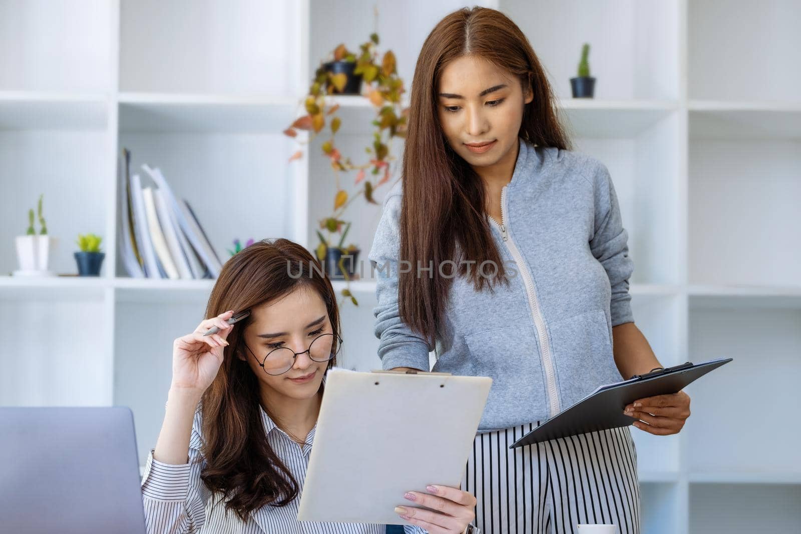 Businesswomen and colleagues are using budget document to calculate last quarter earnings of the year to plan financial investments for the coming year. by Manastrong