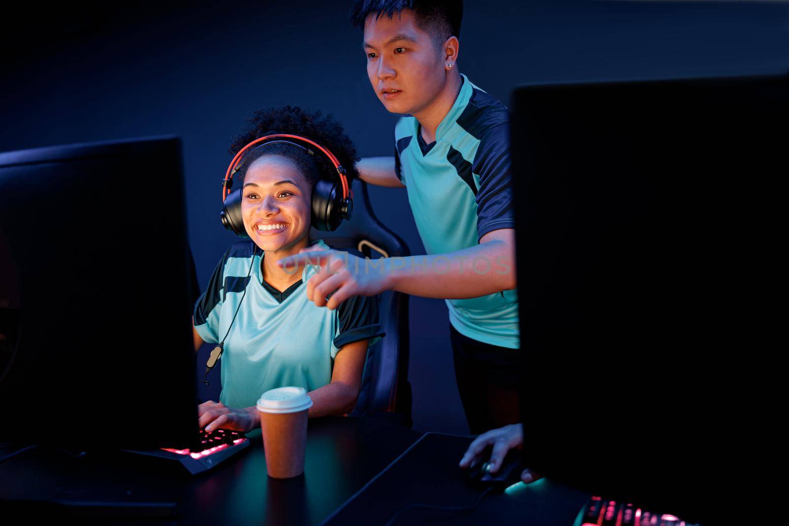 Happy female esports player concentrated on game while friend assisting her to pass network game in internet club