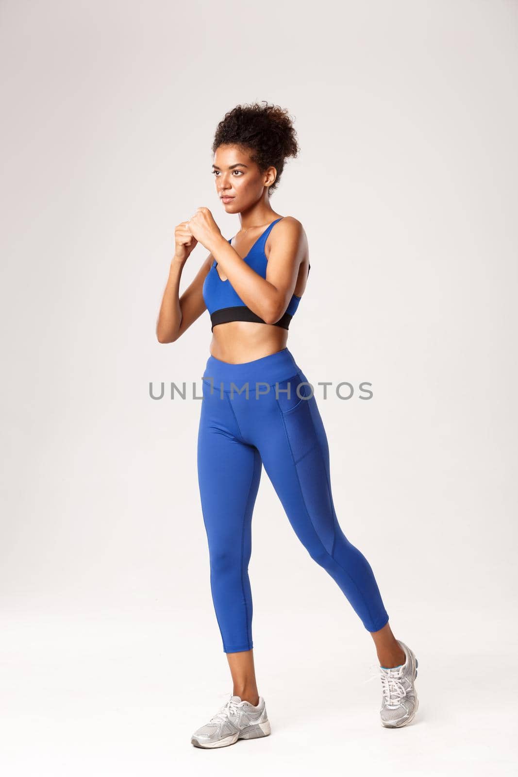 Full length of serious african american sportswoman in blue sportswear practice box punches, shadowboxing and workout over white background by Benzoix