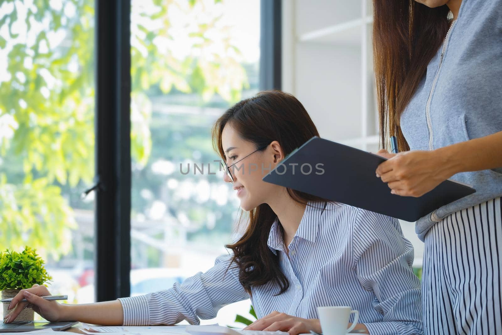Businesswomen and colleagues are using computers to calculate last quarter earnings of the year to plan financial investments for the coming year. by Manastrong