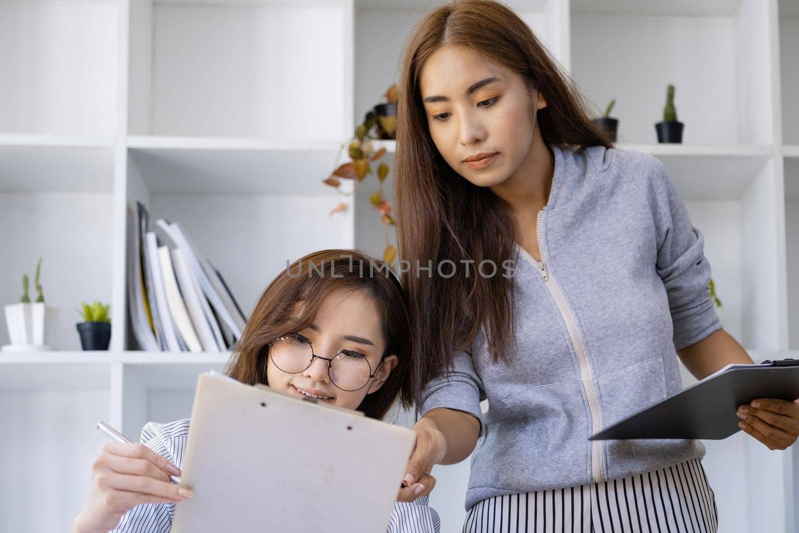 Businesswomen and colleagues are using budget document to calculate last quarter earnings of the year to plan financial investments for the coming year. by Manastrong