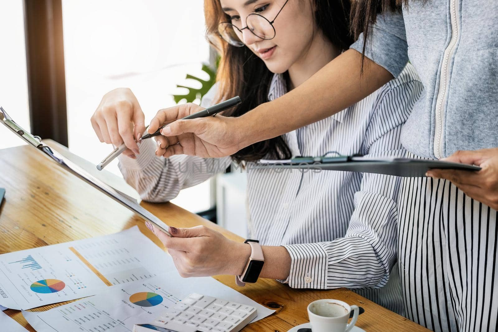 Businesswomen and colleagues are using budget document to calculate last quarter earnings of the year to plan financial investments for the coming year. by Manastrong