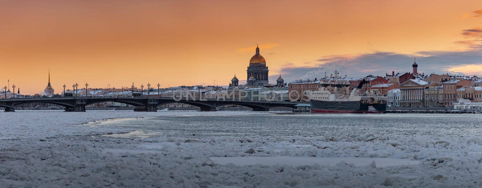 Winter panoramic view of St. Petersburg at sunset, Isaac cathedral and Blagoveshenskiy bridge on background, steam over frozen Neva river, huge ship moored near embankment, sky of orange color. High quality photo