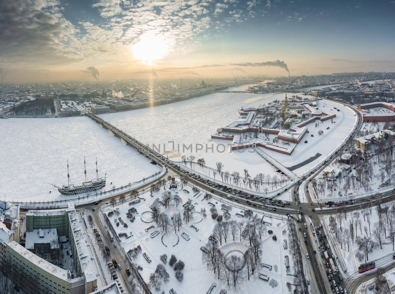 Drone point of view of winter St. Petersburg at sunset, frozen Neva river, steam over city, Peter and Paul fortress, car traffic on Trinity bridge, rostral columns, Palace drawbridge, panoramic view. High quality photo