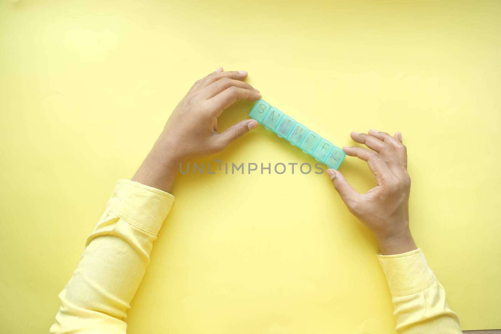 man's hands taking medicine from a pill box on yellow background .