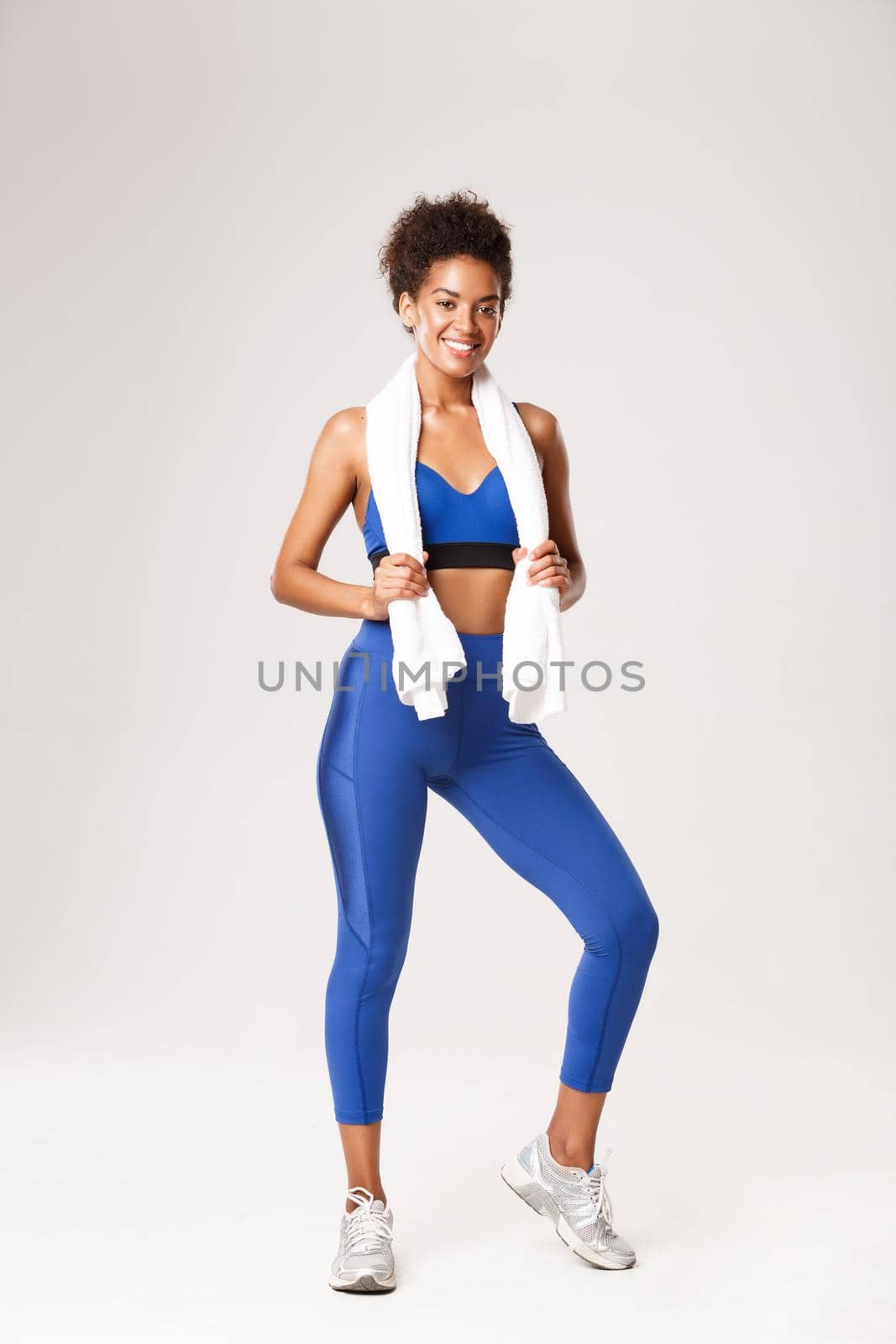 Full length of healthy fit sportswoman in blue uniform, holding towel and smiling pleased after good workout, standing against white background by Benzoix
