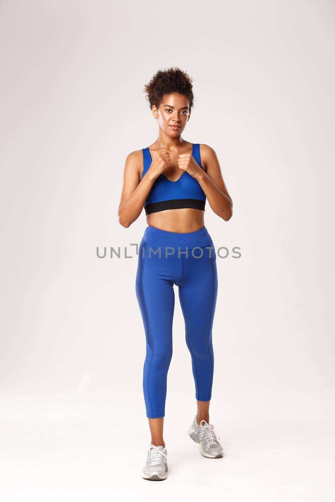 Full length of smiling african-american girl in sportswear, raising hands for fight, boxer workout and practice punches, standing determined over white background.