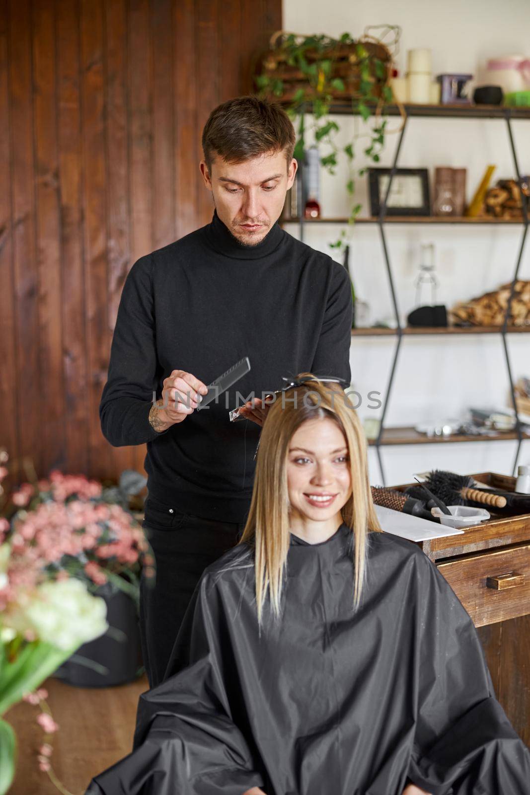 Confident male stylist is dyeing hair of blond caucasian female client