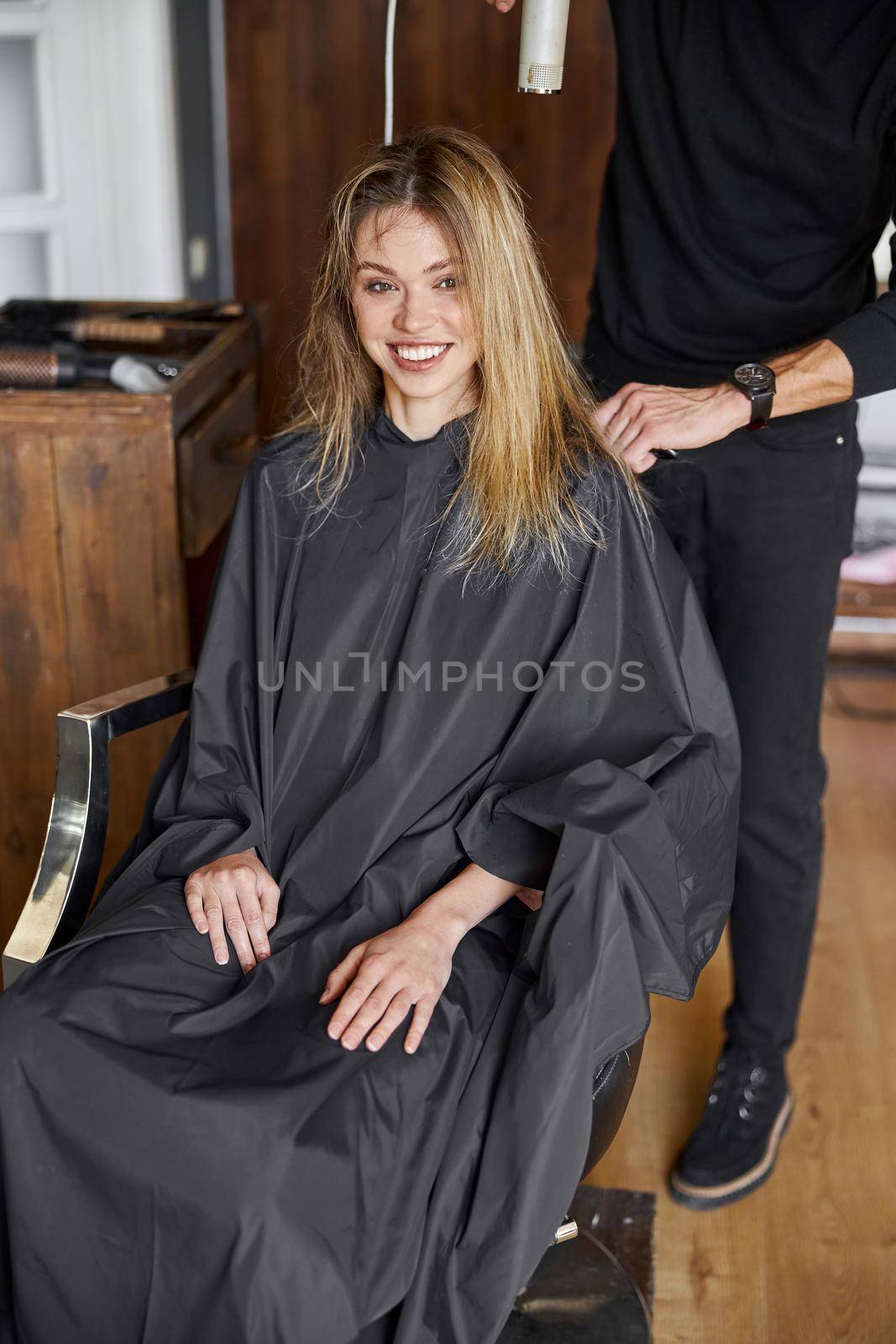 Happy beautiful light hair caucasian woman at beauty salon. Male master is drying her hair by Yaroslav_astakhov