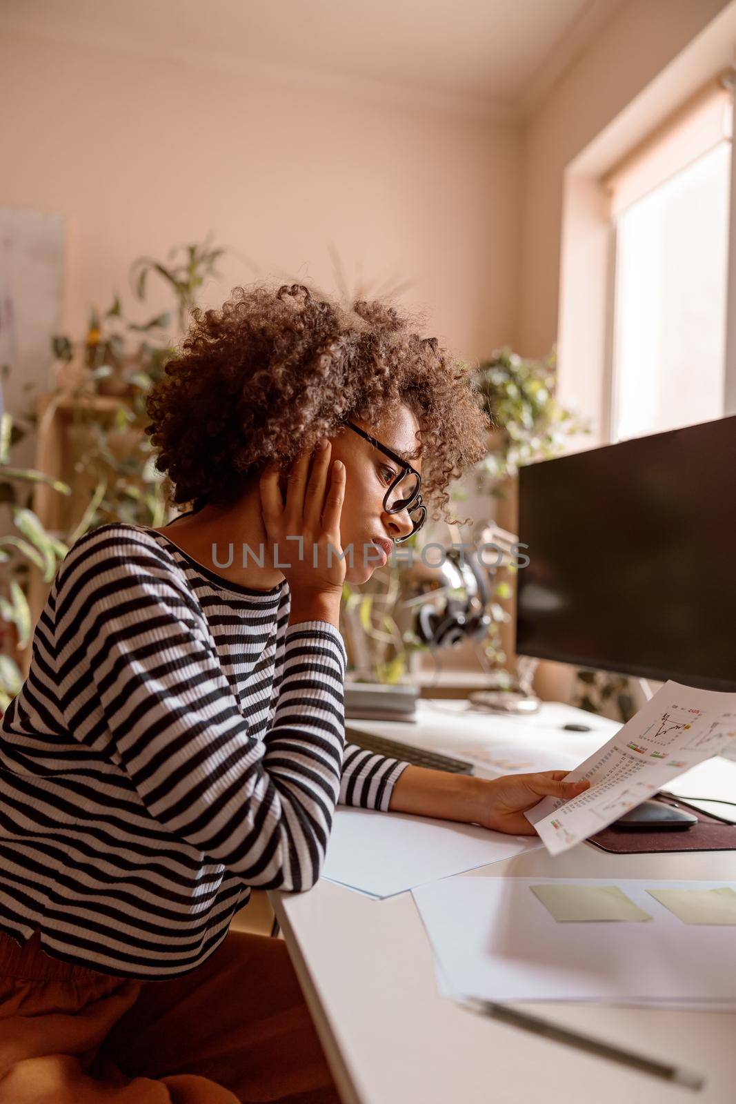 Multiracial lady sitting at the table and analyzing financial papers with graphs while working on project