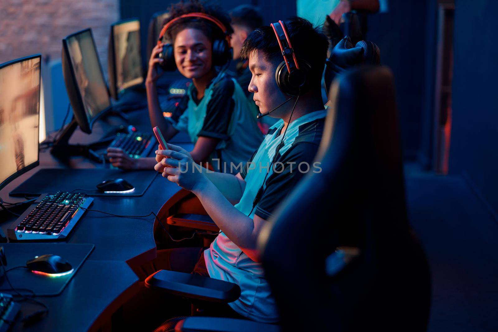 Side view of Asian cybersport gamer in headphones playing mobile game on cellphone in contemporary e-sports club