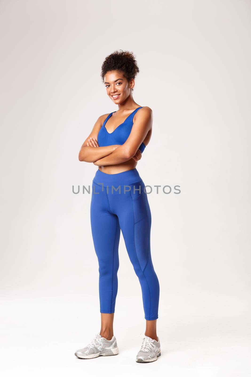 Full length of confident african-american sportswoman smiling pleased at camera, cross arms on chest and looking at camera, wearing sportswear for workout or gym exercises, white background.