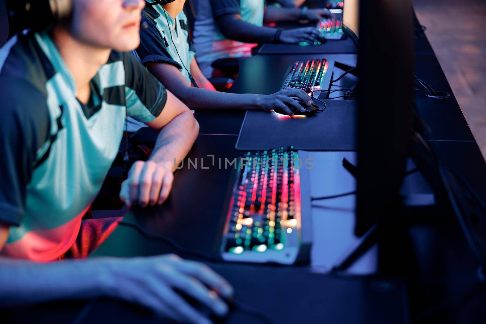 Selective focus on gamers hands using brightly lit keyboards while playing in competitive game in cyber games arena club
