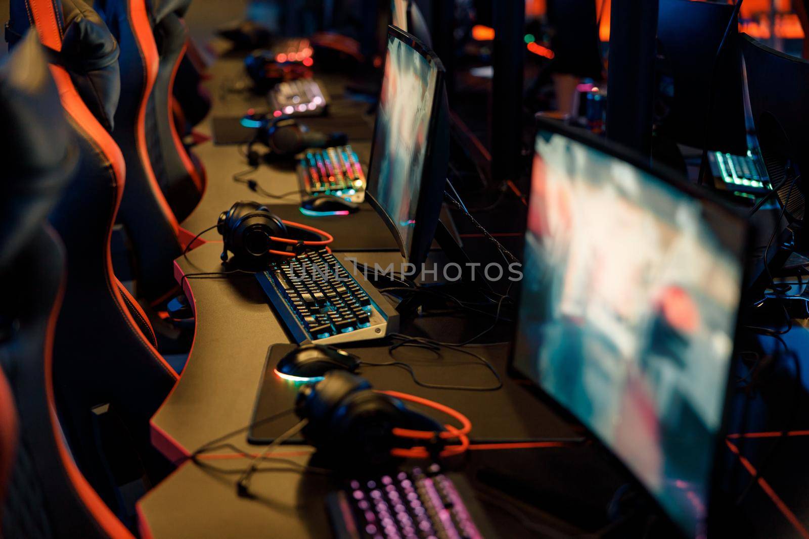 Shot of playing places with row of monitors, headsets and backlit colorful keyboards in dark gaming room